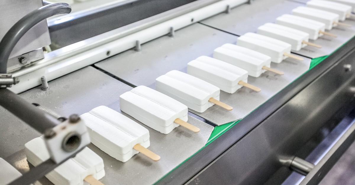Conveyor belt system in a factory setting, displaying the production process of stick ice-cream, with various machines.