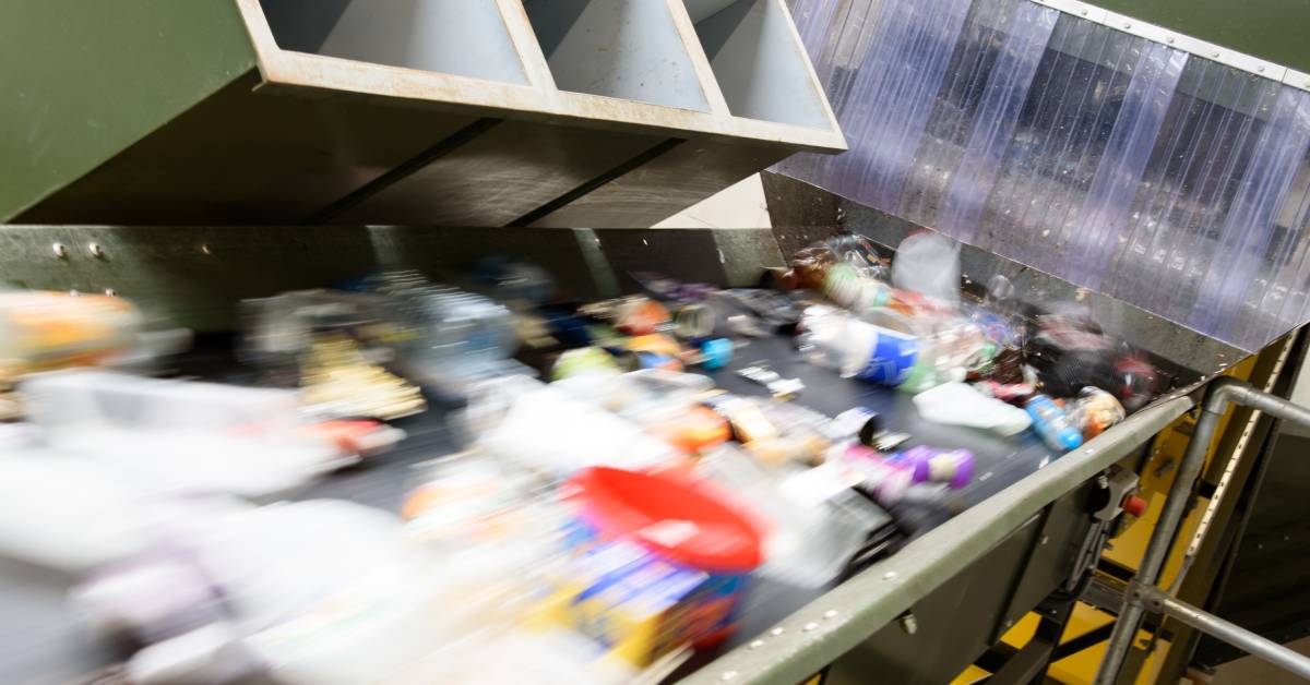 A recycling plant moves various items on a downward angle on a conveyor, including bottles and food containers.