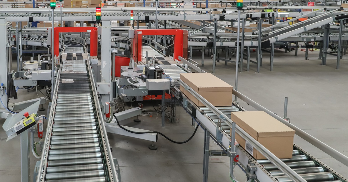 Two conveyor systems sit side by side in a warehouse. One features two packages on its line, while the other is empty.