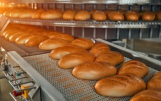 Several freshly baked bread loaves move together on a conveyor system. The controls are visible along the system.