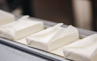Close-up of packages of curd cottage cheese moving along a conveyor system. The paper packaging is white.