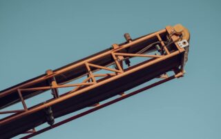 A portable conveyor system points upward in the air. It has an orange metal frame and sits against a blue background.