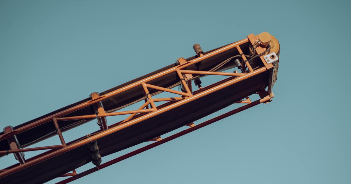 A portable conveyor system points upward in the air. It has an orange metal frame and sits against a blue background.